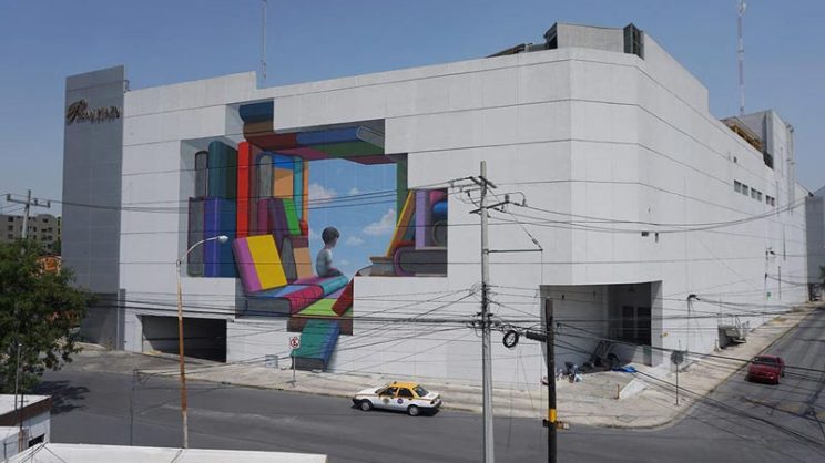 Fresque murale sur un bâtiment représentant un enfant de dos entouré de nombreux livres plus grands que lui. Une ouverture sur le ciel bleu fait face à l'enfant qui regarde vers le bas.