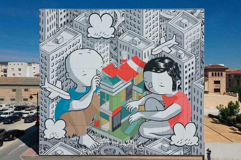 Vue d'immeuble dont la façade est recouverte d'une fresque murale. 2 enfants sont représentés, en train de construire un bâtiment très coloré  comme on construirait une maison en "lego". Autour d'eux, des buildings ternes et uniformes. 